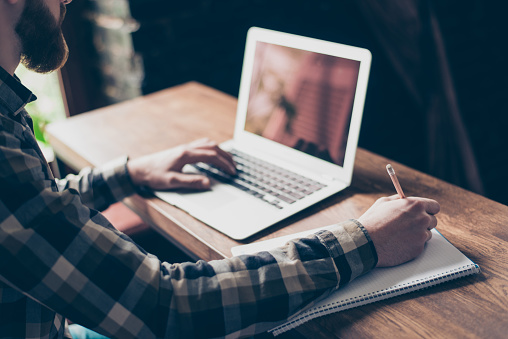 People management employment marketing modern technology concept. Cropped close up photo of smart intelligent focused concentrated clever guy doing home task writing information to copybook